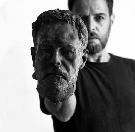 Archival photograph of artist Austin Camilleri inspecting carved stone fragments
